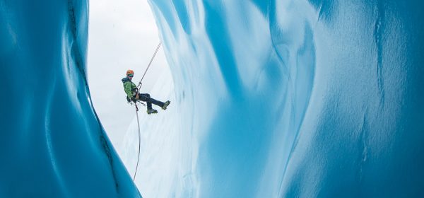 An,Ice,Climber,In,A,Green,Jacket,And,Orange,Helmet